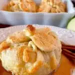 Country Apple Dumpling on a plate with a pool of cinnamon sauce and more apple dumplings in the background