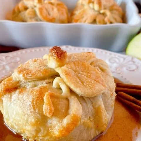 Country Apple Dumpling on a plate with a pool of cinnamon sauce and more apple dumplings in the background