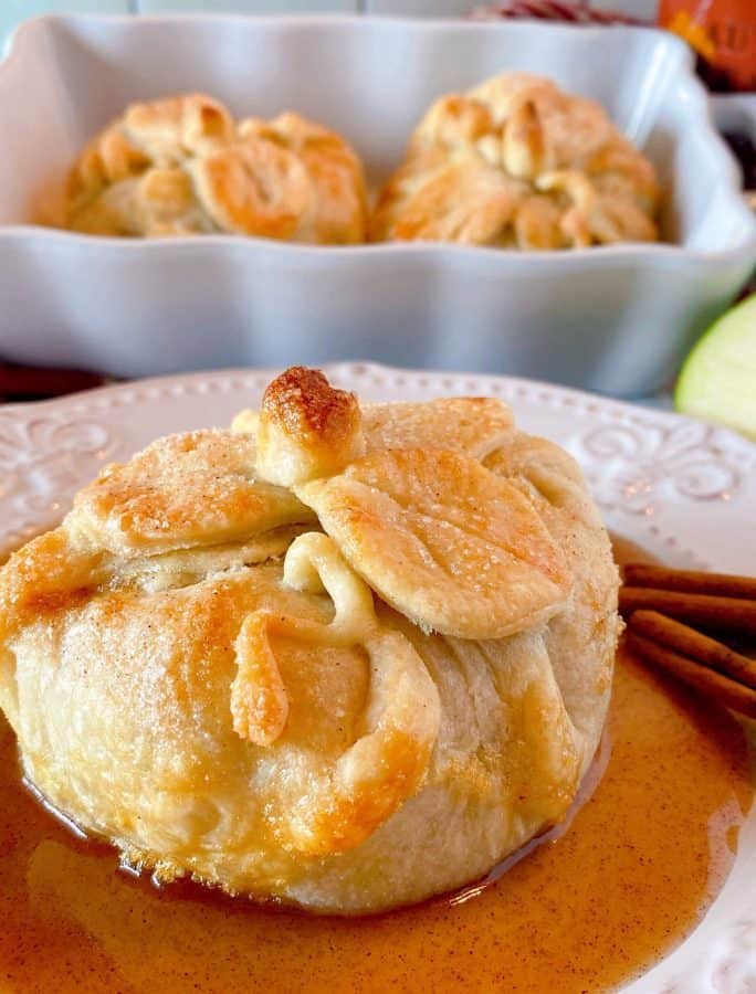 Country Apple Dumpling on a plate with a pool of cinnamon sauce and more apple dumplings in the background