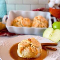 Country Apple Dumpling on a plate with cinnamon sauce and more apple dumplings in a baking dish in the background