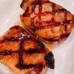 Two Grilled Brown Sugar Glazed Pork Chops on a white plate.