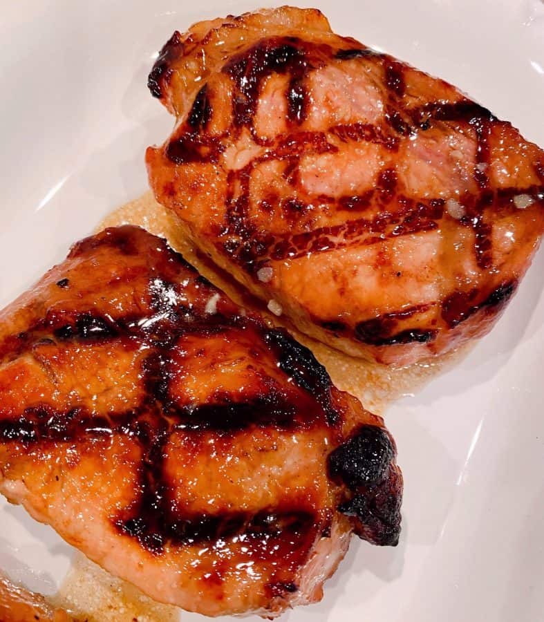 Two Grilled Brown Sugar Glazed Pork Chops on a white plate.