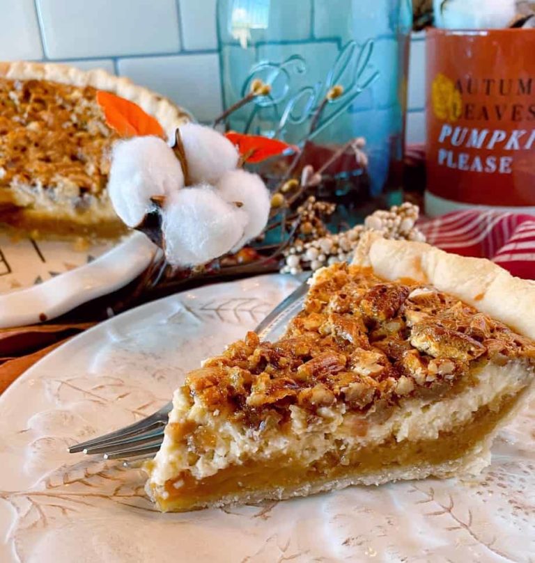 Slice of Caramel Pecan Cheesecake Pie on a tan plate with a fork and whole pie in the background with fall decor.