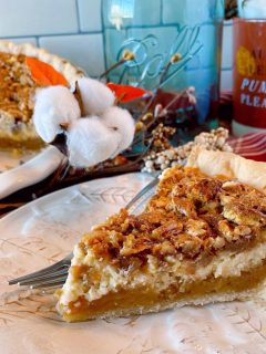 Slice of Caramel Pecan Cheesecake Pie on a tan plate with a fork and whole pie in the background with fall decor.
