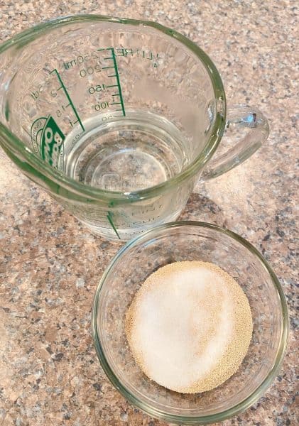 Measuring cup with warm water and a small bowl with yeast.