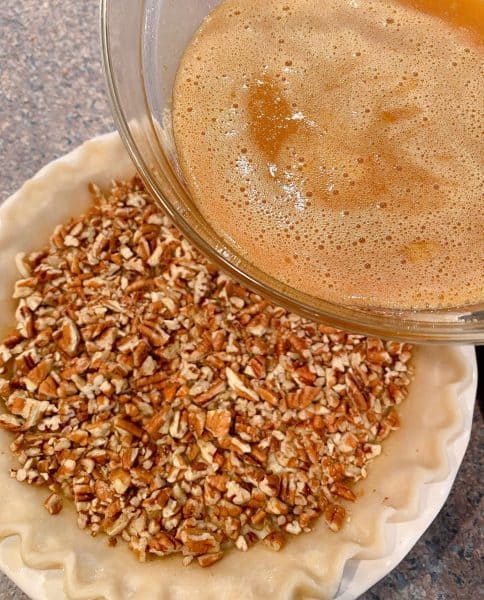 Pouring caramel sauce over pecans in the pie plate.