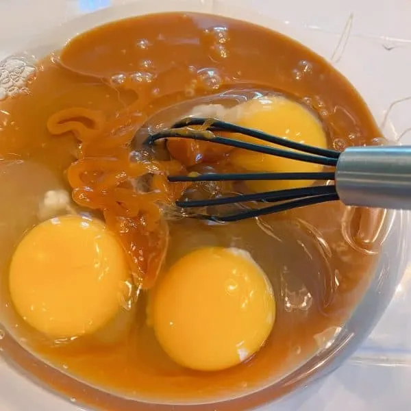 Eggs and caramel ice cream topping in a bowl being whisked together