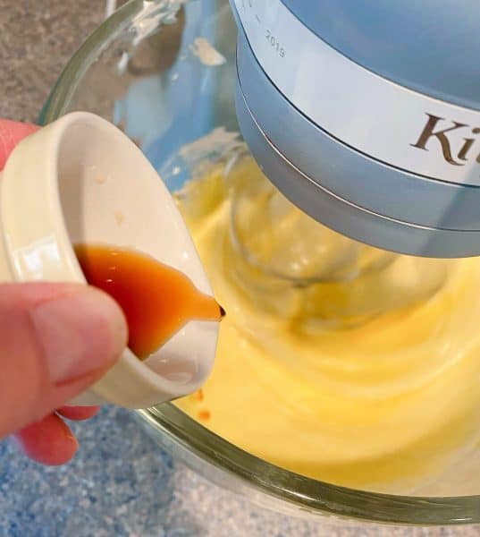 Adding vanilla to cheesecake mixture in the mixing bowl.