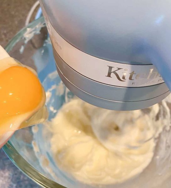 Adding 1 egg to cream cheese mixture in the mixing bowl of a mixer.