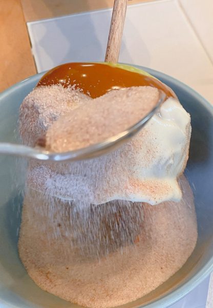 Sprinkling the dipped apples with cinnamon sugar.