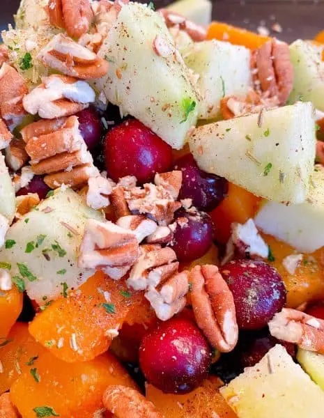 Adding chopped pecans to squash medley on baking sheet.