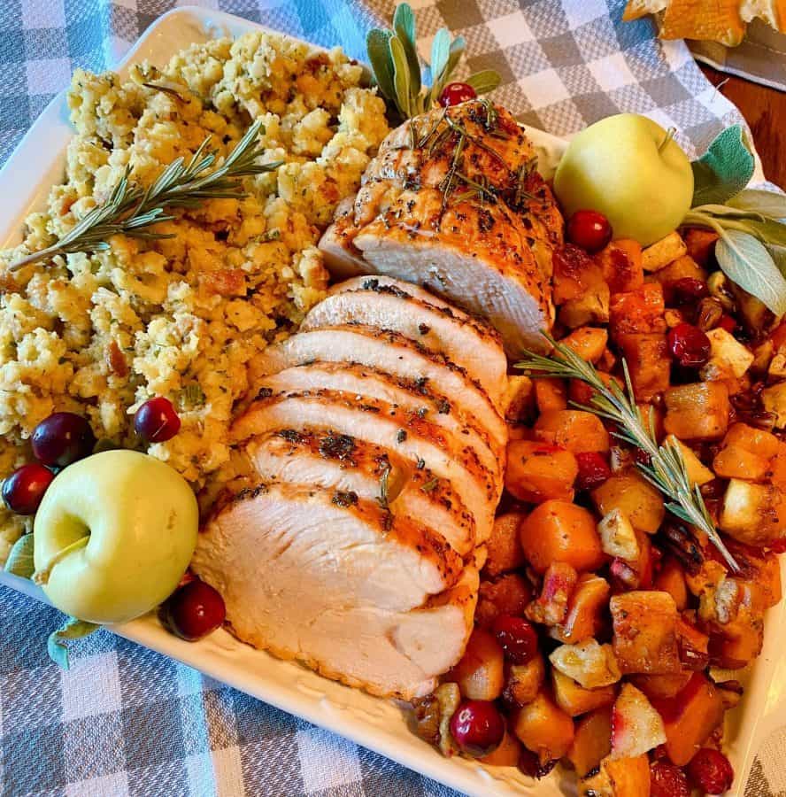 Herb Crusted Turkey Roast on a platter with roasted squash and stuffing. 