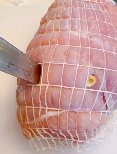 Knife being placed into the turkey roast making slits for garlic.