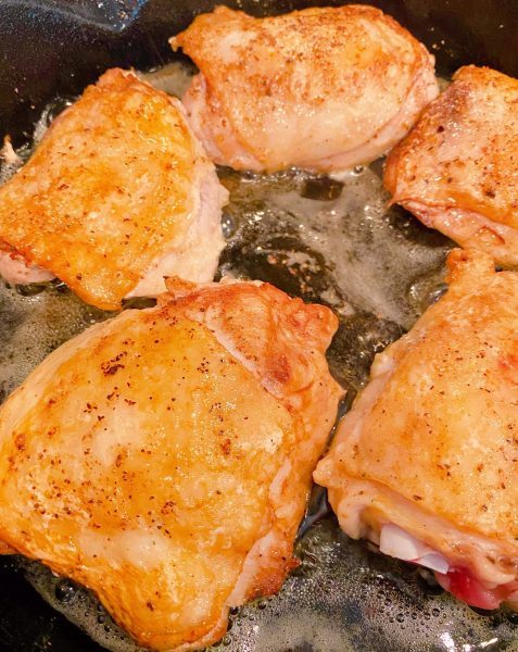 Golden Chicken Thighs frying in skillet.