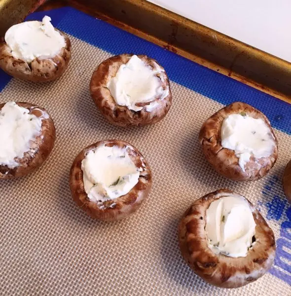 Mushroom caps stuffed with cream cheese on a silicone baking mat.