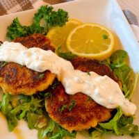 Lump Crab Cakes on a plate with homemade tartar sauce drizzled across the top.