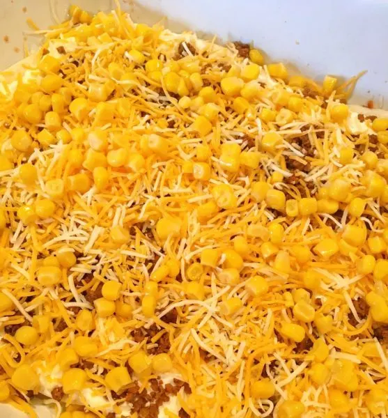 Adding corn and cheese to top of ground meat mixture on Mexican Lasagna Casserole.