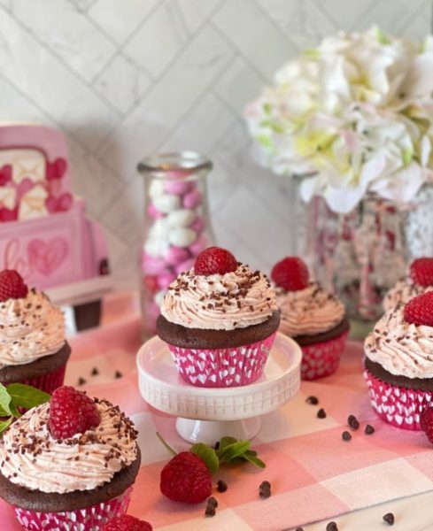 Finished Cupcakes on a pink buffalo table cloth and valentines decorations.