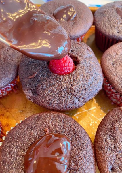 Spooning chocolate ganache over fresh raspberry in the cupcake.