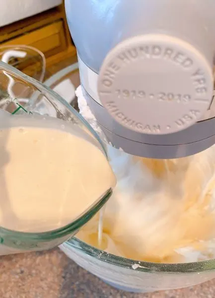 Adding whipping cream to buttercream mixture in the mixing bowl.