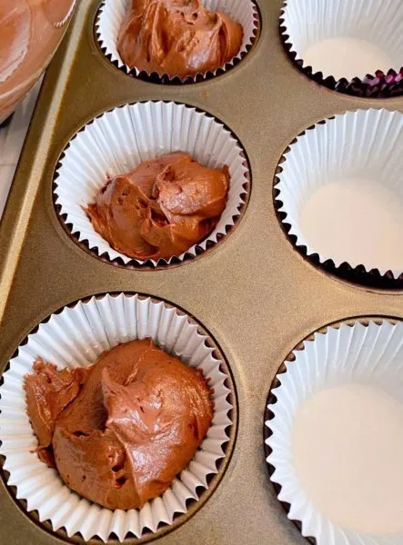 Filling paper lined muffin tin with chocolate cake filling. 
