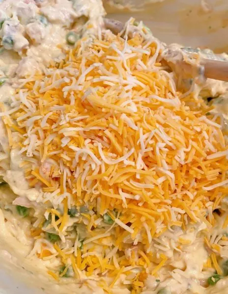 Combing casserole ingredients with grated cheese in the bowl
