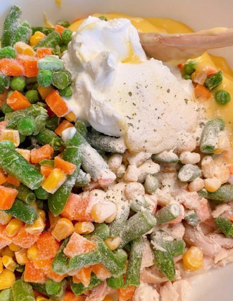 Adding frozen vegetables and sour cream to casserole ingredients.