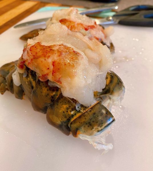 Lobster meat lifted out of shell and resting on top of closed lobster shell.