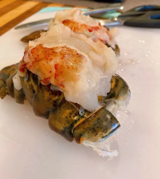 Lobster meat lifted out of shell and resting on top of closed lobster shell.