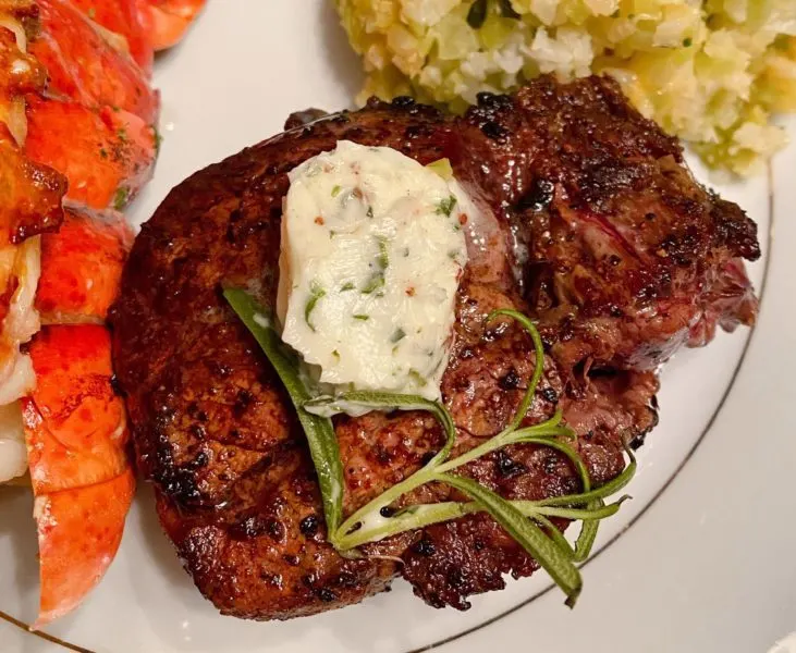 Filet Mignon Steak on a pretty china plate with a pat of herbed butter and a garnish of fresh rosemary.
