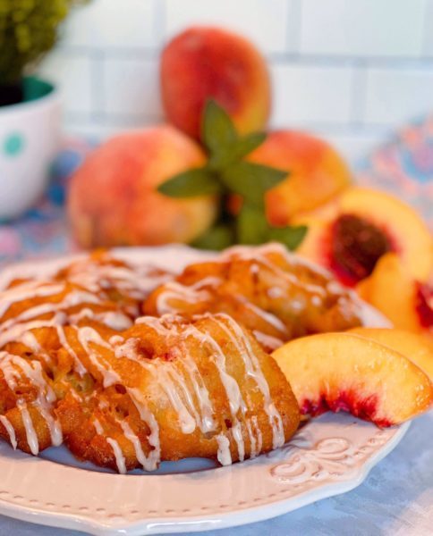 Plate full of Peach Fritters with fresh peaches in the background