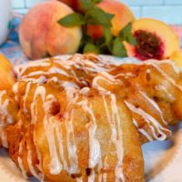 Fried Peach Fritters on a plate with fresh peaches in the background.