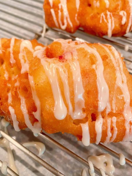 Peach Fritter on a cooling rack with wax papper underneath to catch the glaze that runs off the fritters after glazing.