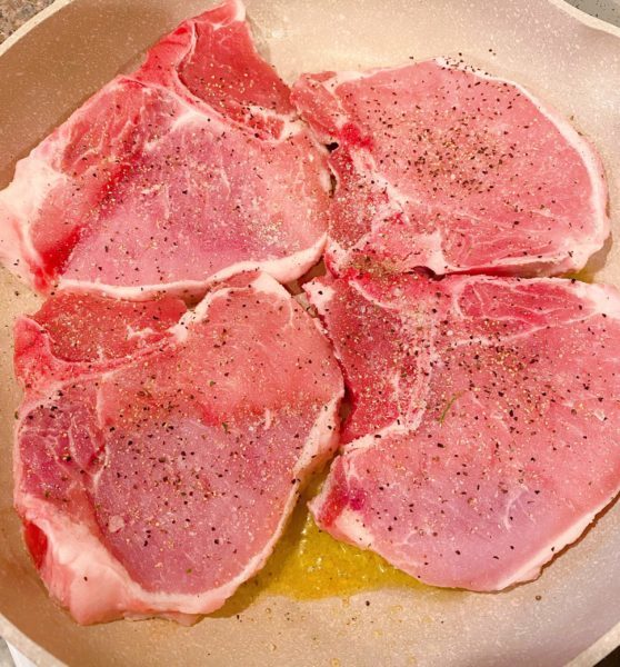 Four bone in pork chops in hot skillet browning on the range.