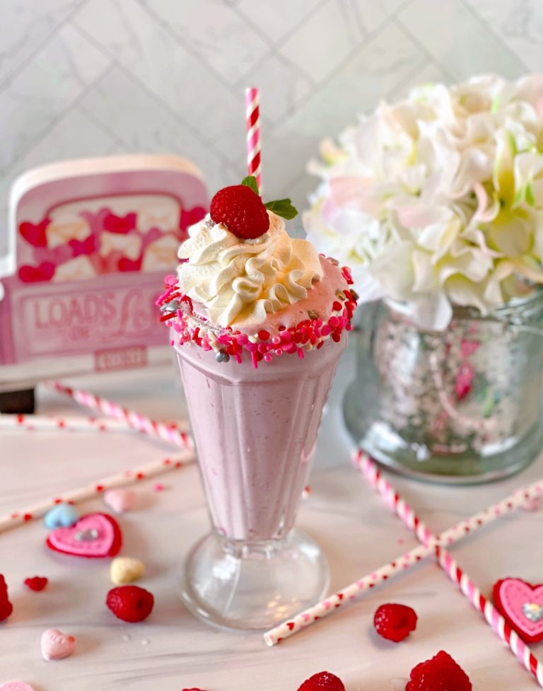 White Chocolate Raspberry Milk Shake in an old fashioned glass rimmed with valentine sprinkles, a festive striped straw, and valentines candies.