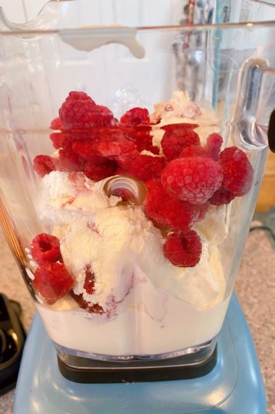 Adding ice cream and frozen raspberries to the blender with the milk.