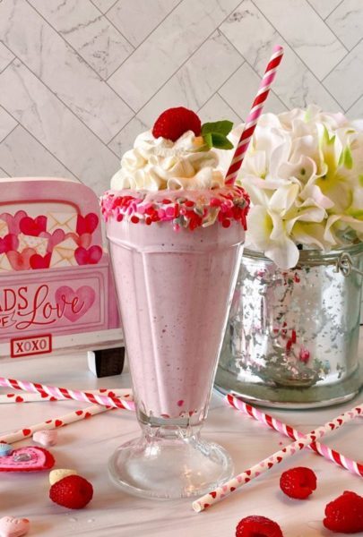 White Chocolate Raspberry Milkshake in a beautifully rimmed glass with sprinkles and a festive straw.