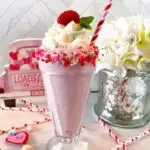 White Chocolate Raspberry Milkshake in an old fashioned glass topped with whipped cream and a fresh raspberry.