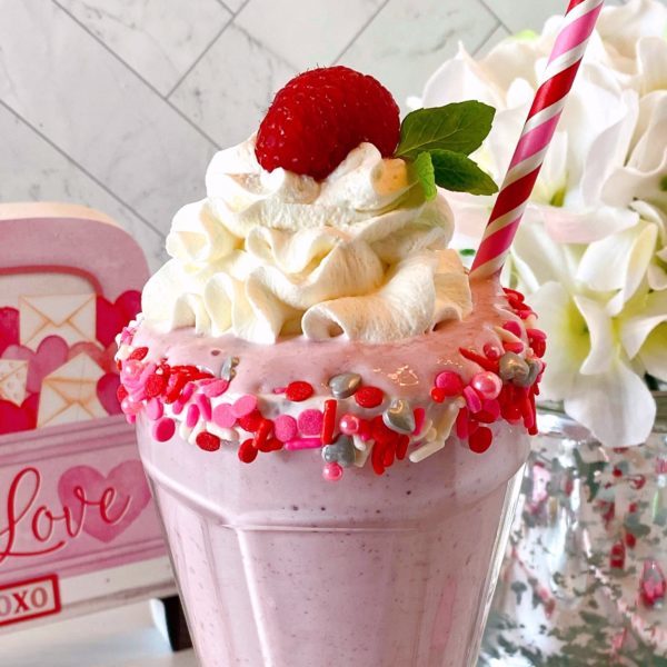 Milkshake topped off with whipped cream, a fresh raspberry, and a sprig of mint.