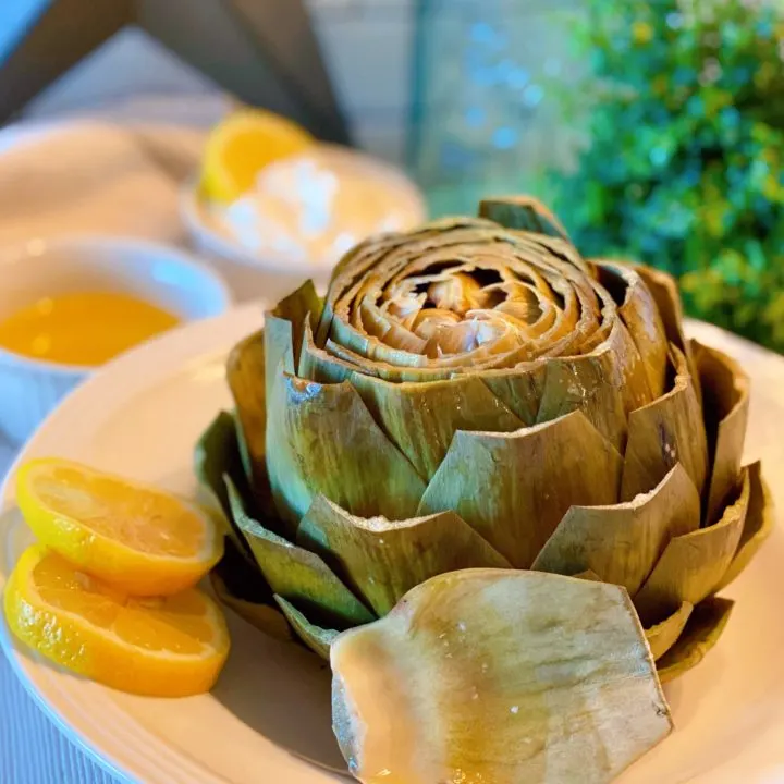 Steamed Artichoke with lemon slices in a serving bowl.