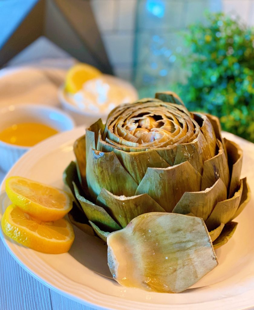 Steamed Artichoke with lemon slices in a serving bowl.