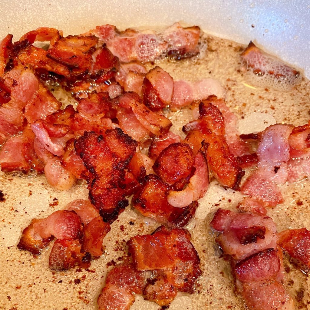 Bacon bits fried up in a skillet over a hot stove top.
