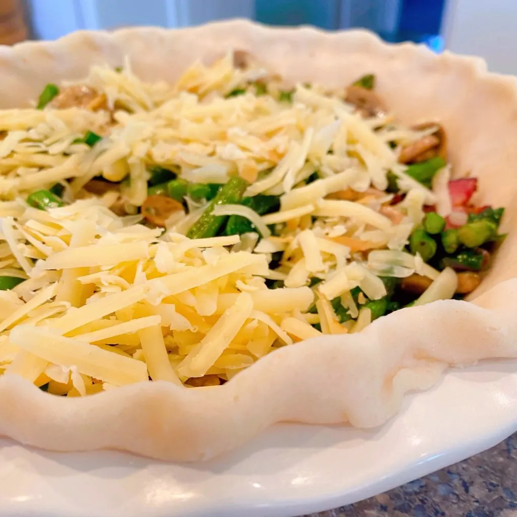 Adding grated cheese to the top of quiche ingredients. 