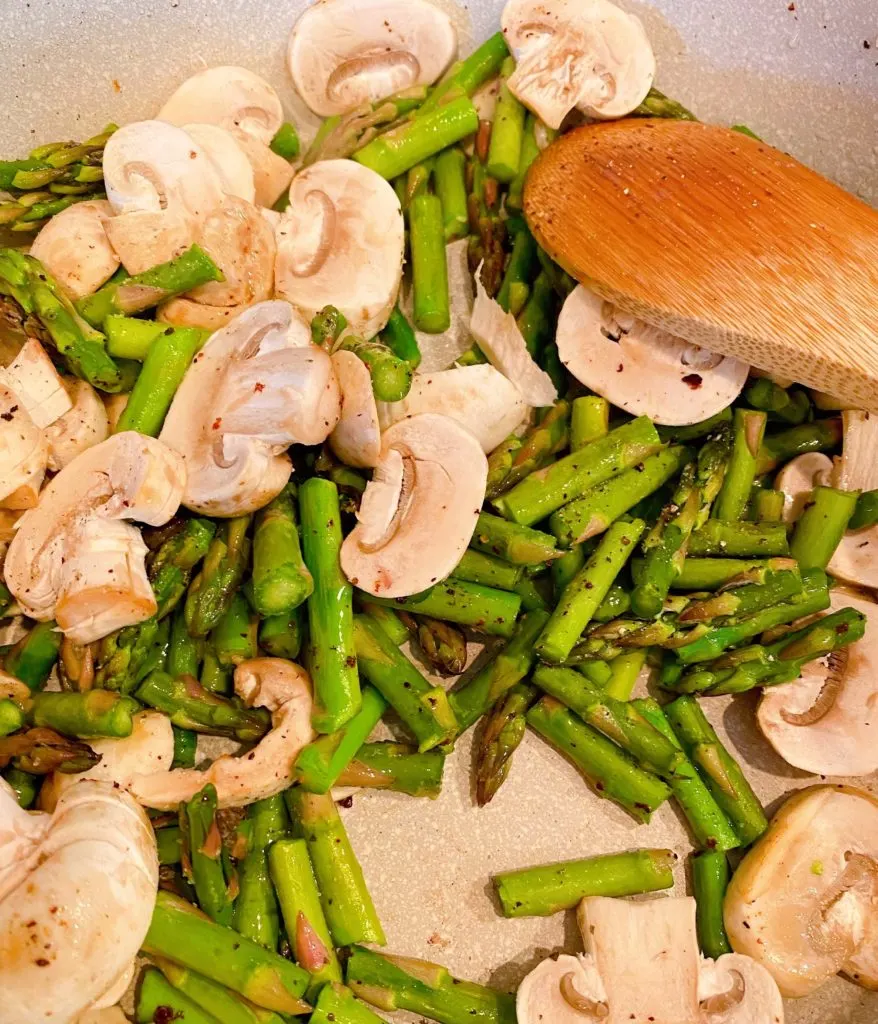 sauteed asparagus and mushrooms in a skillet on the stove top.
