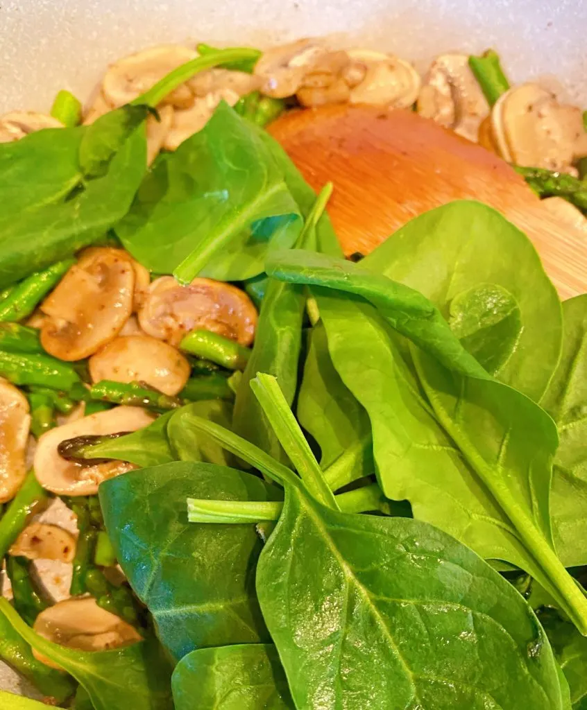 fresh spinach added to asparagus and mushrooms in skillet.