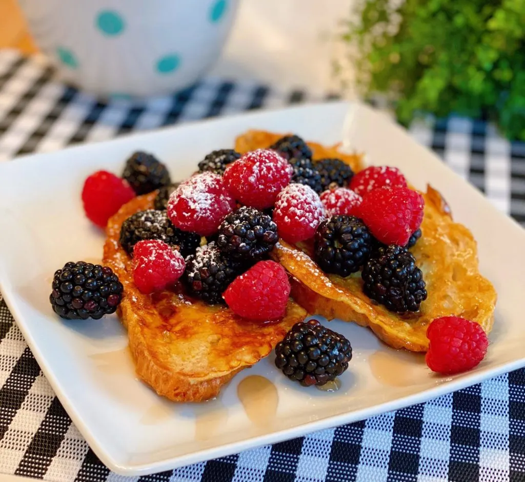 Croissant French Toast on a plate topped with fresh berries and warm maple syrup.
