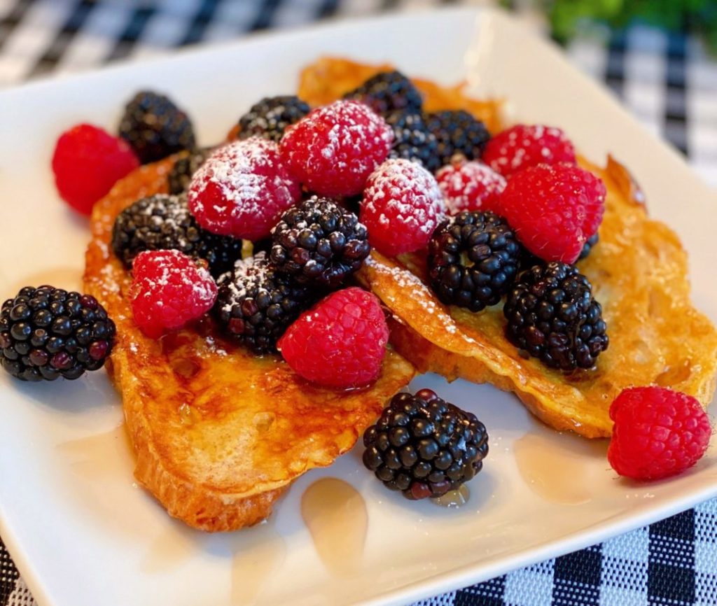 Croissant French Toast with Fresh Berries and Syrup on a white square plate. 