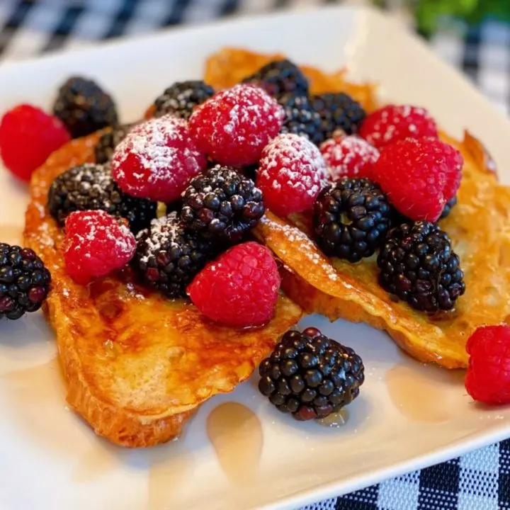 Croissant French Toast with Fresh Berries and Syrup on a white square plate.