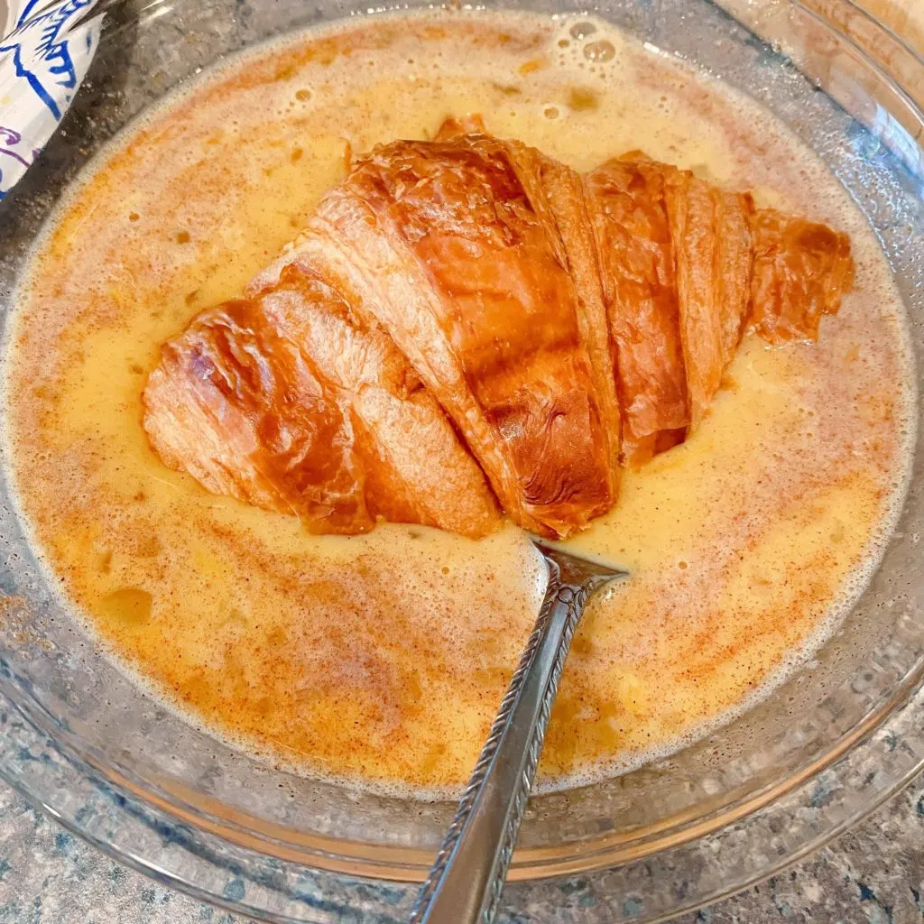 Dunking a croissant into the egg batter. 