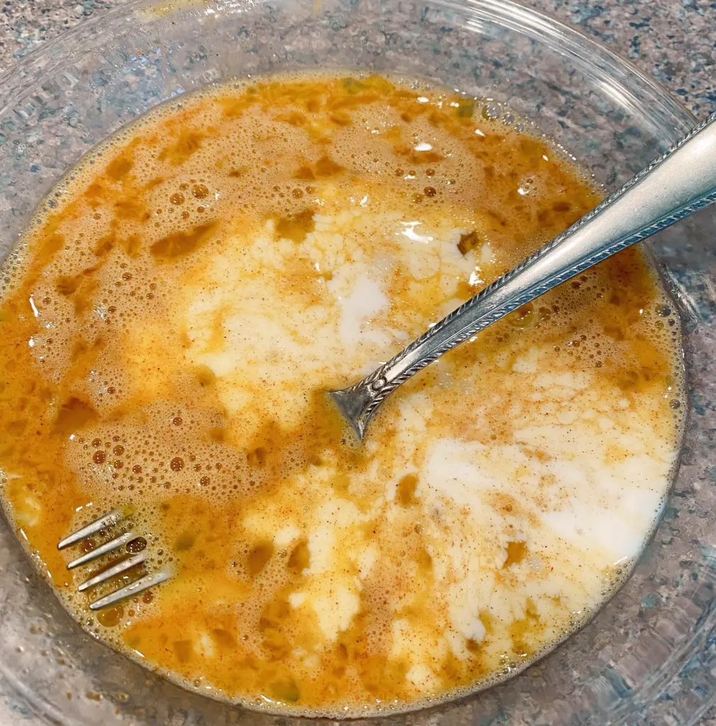 Adding half-and-half to egg mixture in a pie plate with a fork for blending.